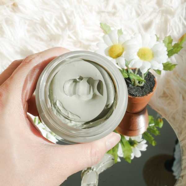 Close-up of a hand holding a clay mask jar, perfect for a calming skincare routine.