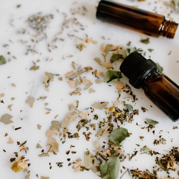 Aromatherapy setup with essential oil bottles and dried herbs on a white surface for holistic healing.